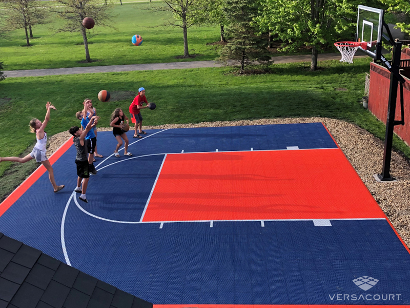 Family playing on a red, white and blue VersaCourt backyard basketball court